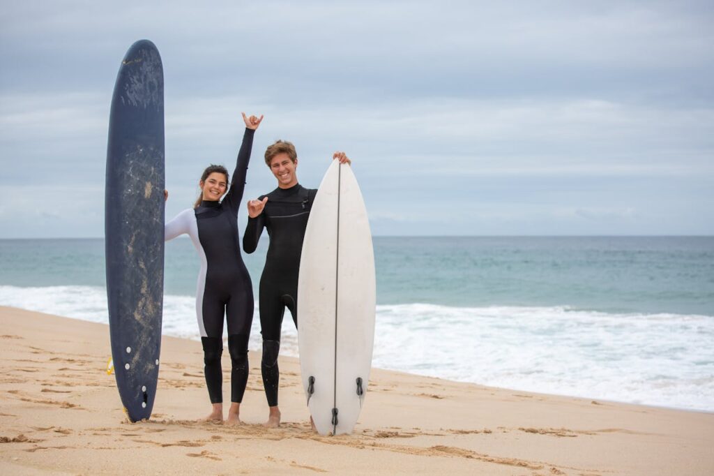 Two young surfers smiling and posing with surfboards on a beach in Portugal.